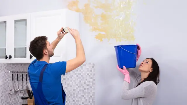 Homeowner photographing a water-stained wall while another holds a bucket